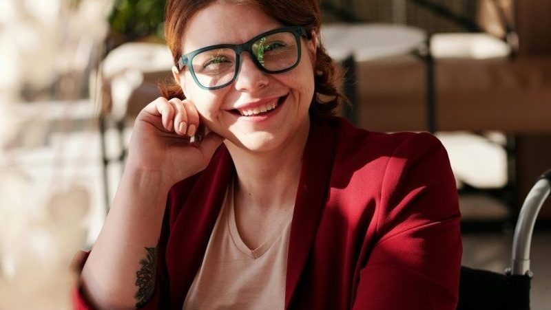 Smiling woman in red blazer working on laptop with coffee and meal at café.